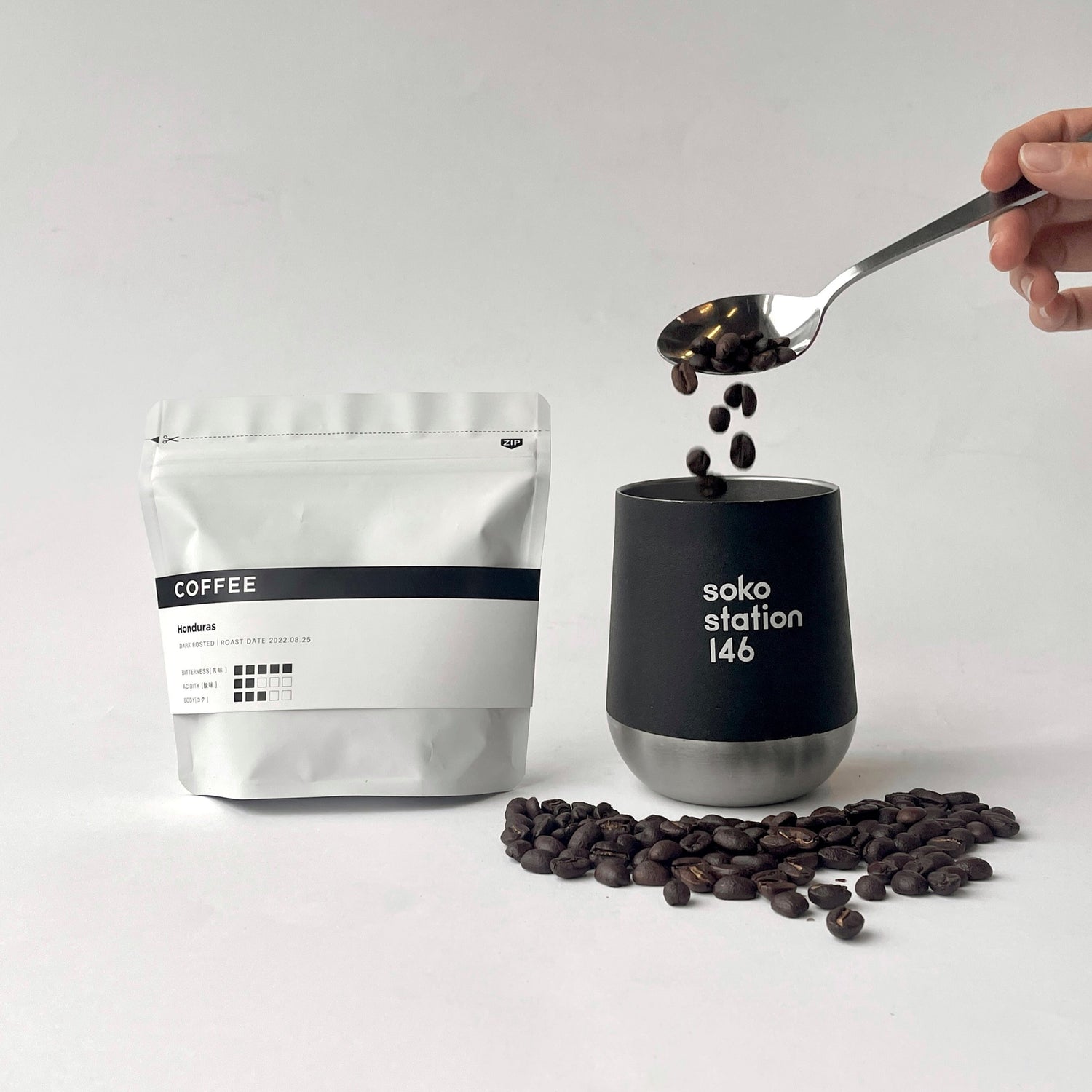 コーヒー豆（2種のうち1種）と、白とシルバーのサーモタンブラーが入ったシンプルでミニマルなデザインのコーヒーギフトセット